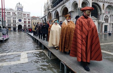Masked revellers walk on raised platforms above flood waters during a period of seasonal high water and on the first day of carnival, in Venice February 1, 2015. REUTERS/Stefano Rellandini