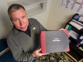 Reverend John Wilcox holds a Parish Register similar to the ones that were stolen inside  a safe from the church office at St. Mary's Church in Navan. (The safe used to be under the TV in the bottom left of photo.) 
Errol McGihon/Ottawa Sun/QMI Agency