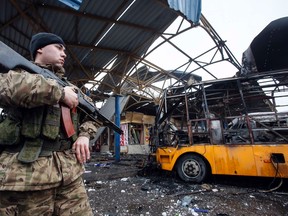 A member of the armed forces of the separatist self-proclaimed Donetsk People's Republic stands guard near a destroyed vehicle at a bus station after shelling in Donetsk, February 11, 2015. REUTERS/Maxim Shemetov