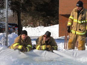 While firefighter Mark Brisseau looks on, cohorts Matt Rumas, left, and Kyle Smith - who volunteered their time - pour 44,000 litres of water to form the base for the new outdoor community skating rink between Msgr. Morrison and Locke's schools. The rink will officially open Monday, Family Day.
