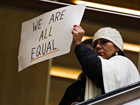 A protester carries a sign down the escalator during an Idle No More round dance to stop racial profiling at City Centre Mall in Edmonton, Alta., on Saturday, Nov. 8, 2014. Respected aboriginal elder Gary Moostoos was banned from the mall last month. Oxford Properties Group later rescinded the ban and apologized to Moostoos. Codie McLachlan/Edmonton Sun/QMI Agency