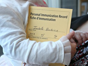 Melanie Lauziere holds her daughter Isabelle after she got her immunized at the Montfort Hospital on Friday Feb 13, 2015. Isabelle holds her immunization record.  Tony Caldwell/Ottawa Sun/QMI Agency