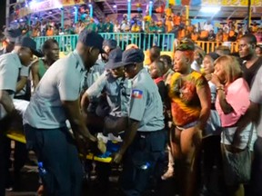 People look at an injured person being carried away after a carnival float hit power lines, on the second day of the annual Carnival celebrations in Haiti's capital Port-au-Prince in this February 17, 2015 still image taken from Reuters TV. At least 18 people were killed and 60 injured early on Tuesday when the carnival float hit power lines. The float caught fire after it hit a high-voltage overhead power cable, witnesses said. REUTERS/Reuters TV