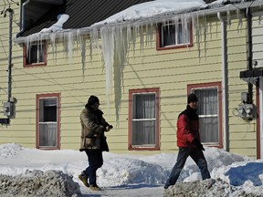 Terry Marchant and William Runions walk past a large icicle hanging from a home on Raglan Road. (Julien Gignac/For The Whig-Standard)