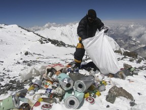 This picture taken on May 23, 2010 shows a Nepalese sherpa collecting garbage, left by climbers, at an altitude of 8,000 metres during the Everest clean-up expedition at Mount Everest.  Climbers scaling Mount Everest will have to bring back eight kilograms (17.6 pounds) of garbage under new rules designed to clean up the world's highest peak, a Nepalese official said March 3, 2014.    AFP PHOTO/Namgyal SHERPA/FILES