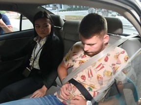 A policewoman sits next to Elton Hinz, one of the two German nationals arrested in Singapore for vandalism, as they arrive in a police car to the state court on November 22, 2014. Two German men were arrested in Singapore on November 21 for spray-painting graffiti on a metro train in the city-state, an offence punishable by flogging with a wooden cane. AFP PHOTO/ROSLAN RAHMAN