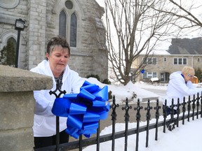 Margie Robb pins a blue ribbon on a fence across the street from Nicholson Catholic College.