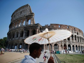 A vendor holds up a Chinese paper umbrella on a hot summer day in front of Rome's ancient Colosseum July 28, 2013. (REUTERS/Tony Gentile)
