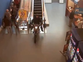 A motorcyclist burns down an escalator in a Surrey, B.C. mall on Feb. 20, 2015, during a wild police chase, video of which has made its way to the Internet. (Screenshot from YouTube video)