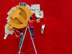 Workers peel newspaper off a wall after repainting the hammer and sickle symbol of the Chinese Communist Party flag on it at the Nanhu Revolutionary Memorial museum in Jiaxing, Zhejiang province, in this May 21, 2014 file photo. REUTERS/Chance Chan/Files