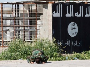 A member of militias known as Hashid Shaabi kneels as he celebrates victory next to a wall painted with the black flag commonly used by Islamic State militants, in the town of al-Alam on March 10, 2015. (REUTERS/Thaier Al-Sudani)