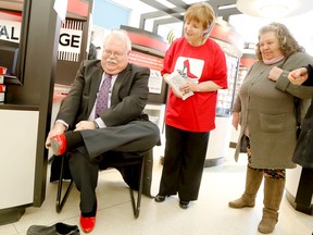 Connie Carson and Sandy Watson-Moyles watch as Gerry Drage puts on his red high heels during the Walk A Mile In Her Shoes promotion held at the Quinte Mall, March 26, 2015. The walk through downtown is scheduled for May 9. 
Emily Mountney/Belleville Intelligencer/QMI Agency