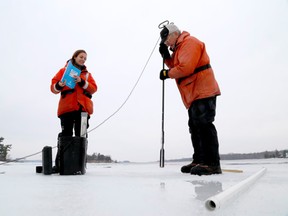 Queen's University masters student Colleen Burliuk waits for professor John Casselman to complete chipping a hole in the ice on the St. Lawrence River so data can be collected in a location where an American eel is wintering in a burrow earlier this week near Rockport.