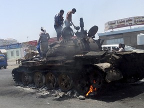 People stand on a tank that was burnt during clashes on a street in Yemen's southern port city of Aden March 29, 2015. REUTERS/Stringer