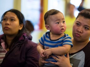 Temporary foreign workers Anna Lou (left) and Grizal Marron (right, with her 9-month-old son Ghian) listen to speeches during a rally held in support of temporary foreign workers at the Panciteria De Manila restaurant in Edmonton, Alta., on Tuesday, March 31, 2015. The federal government has set a deadline of April 1, when permits expire for temporary foreign workers who have been in Canada for more than four years. Ian Kucerak/Edmonton Sun/ QMI Agency