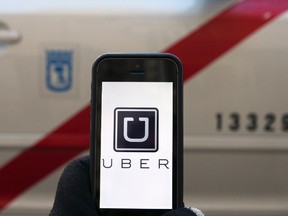 The logo of car-sharing service app Uber on a smartphone in front of a taxi is seen in this photo illustration taken in Madrid on December 10, 2014. (REUTERS/Sergio Perez)