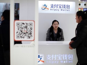 A sales assistant sits behind and under Alipay logos at a train station in Shanghai, Feb. 9, 2015. REUTERS/ALY SONG
