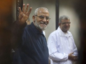 Muslim Brotherhood's Supreme Guide Mohamed Badie (L) flashes the Rabaa sign as he stands behind bars during his trial with ousted Egyptian President Mohamed Mursi and other leaders of the brotherhood at a court in the police academy on the outskirts of Cairo in this December 14, 2014 file photo. An Egyptian court on April 11, 2015 sentenced Badie, leader of the outlawed Muslim Brotherhood, and 13 other senior members of the group to death for inciting chaos and violence, and gave a life term to a U.S.-Egyptian citizen for ties to the Brotherhood.  REUTERS/Asmaa Waguih/Files