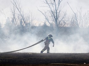 A firefighter drags a hose towards a grass fire above the skateboard park in Muskoseepi Park in 2015. FILE PHOTO