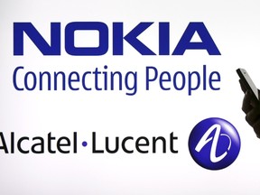 A woman holds a smartphone in front of a screen displaying both Nokia and Alcatel Lucent logos in this photo illustration in Paris, April 14, 2015. REUTERS/Benoit Tessier
