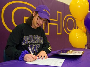 Charlotte Prouse, a prolific distance runner, puts her signature on the papers in the Central secondary school gym Wednesday to officially commit to the University of Washington. At left, Prouse gets a hug from coach Jackie Trudeau. (Mike Hensen, The London Free Press)