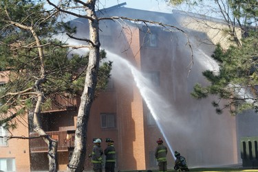 Firefighters at ground level work to contain a four-alarm apartment complex fire in West Ottawa on Saturday. Strong winds swept the flames quickly through the upper floor of the Deerfield Dr. townhome complex. (MICHAEL MILLER Submitted Image / Ottawa Sun)