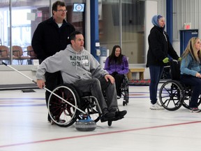 Ted Bergeron, in black jacket, and Gavin Cosgrove of Bergeron Clifford LPP, sponsors of the event, try their hand at adaptive curling at the third annual Adaptive Curling Bonspiel. (Steph Crosier, The Whig-Standard, Postmedia Network)