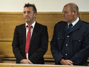 Former AC/DC drummer Phil Rudd (L) stands in in the dock flanked by security facing charges at the District Court in Tauranga, New Zealand on April 21, 2015. The veteran rocker made  a  surprise guilty plea on charges of threatening to kill and drug possession.  Rudd, 60,  had previously denied all allegations against him, but changed his plea on the first day of the trial at Tauranga District Court. Judge Robert Woolff adjourned the matter after just 10 minutes and extended Rudd's bail until a sentencing hearing on June 26th.  AFP PHOTO / MARTY MELVILLE