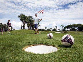 Patrick Wooten (centre) holds the flag as his son Thomas, 11, misses his putt on the second half of the FootGolf course at Largo Golf Course in Largo, Fla., on April 11, 2015. (Scott Audette/Reuters)