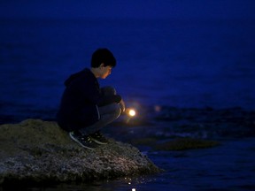 A boy places a candle on the shoreline rocks during a vigil last week to commemorate migrants who died at sea in Sliema, outside the Maltese capital Valletta. European Union leaders who decided last year to halt the rescue of migrants trying to cross the Mediterranean reversed their decision Thursday at a summit hastily convened after nearly 2,000 people died at sea.  (Darrin Zammit Lupi/Reuters)