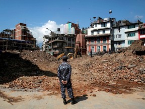 A member of Nepalese police personnel looks on as an excavator is used to dig through rubble to search for bodies, in the aftermath of Saturday's earthquake in Kathmandu, Nepal, April 27, 2015. REUTERS/Danish Siddiqui