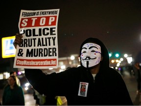 A protestor wearing a Guy Fawkes mask holds a sign as demonstrators march through the streets of Ferguson, Missouri, March 12, 2015. The shooting of two police officers in Ferguson, Missouri, during a protest rally sparked an intense manhunt for suspects on Thursday and ratcheted up tensions in a city at the center of a national debate over race and policing.  REUTERS/Jim Youngé File photo
