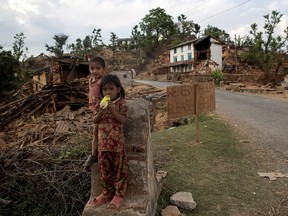 Children stand on a structure of a collapsed house next to signage in a village after an earthquake in Sindhupalchowk, Nepal, May 2, 2015. REUTERS/Danish Siddiqui