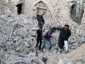 Residents walk amid debris in a site damaged by what activists said was a barrel bomb dropped by forces loyal to Syria's President Bashar al-Assad in the Al-Qtanh neighbourhood of Aleppo, May 1, 2015. REUTERS/Mahmoud Hebbo