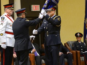 Retired London police Chief Brad Duncan passes a ceremonial flag to new Chief John Pare Monday. MORRIS LAMONT / THE LONDON FREE PRESS