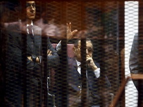 Egypt's former president Hosni Mubarak waves to his supporters with his sons Gamal, left, and Alaa, right, inside a cage in a courtroom during their trial at the police academy, on the outskirts of Cairo, May 9, 2015. (REUTERS/Amr Abdallah Dalsh)