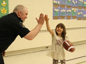 Greater Sudbury Police Const. Matthew Hall, vice-president of the Joe MacDonald Youth Football League, gives Callie Windsor, 6, a high five during a drill at a football clinic conducted by the Greater Sudbury Police and the Joe MacDonald Youth Football League at Queen Elizabeth II Public School in Sudbury, Ont. on Tuesday May 12, 2015. The event was part of Police Week activities. John Lappa/Sudbury Star/Postmedia Network