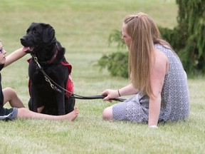 Owen Scott, an eight-year-old non-verbal autistic child, sits in the grass with his autism assistance guide dog, Rowdy, and his mother, Jane Houghton, at their family home near Glencoe. (CRAIG GLOVER, The London Free Press)