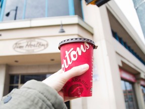 A woman holds a cup of coffee in front of a Tim Hortons in St. Catharines, Ont., in this file photo. (Julie Jocsak/Postmedia Network)