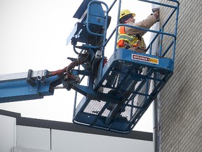 A worker secures a piece of metal siding hanging from the new police headquarters at 266 Graham Ave. on Jan. 22. Work to repair the building will begin soon. (Brian Donogh/Winnipeg Sun file photo)