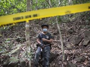 A policeman monitors as forensic experts dig out human remains near the abandoned trafficking camp in the jungle close the Thailand border at Bukit Wang Burma in northern Malaysia on May 26, 2015. (REUTERS/Damir Sagolj)