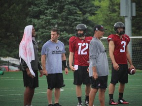 Henry Burris protects himself from the rain in a gathering of quarterbacks Thomas DeMarco, Derek Wendel (12) and Hugo Richard with coach Don Yanowsky during Day 2 of RedBlacks rookie  camp Thursday at Carleton University. (Tim Baines/Ottawa Sun)
