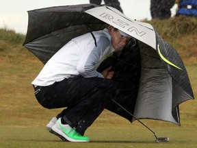 Rory McIlroy shelters from the rain and wind on the sixth tee during the second round of the Irish Open at the Royal County Down Golf Club in Newcastle, Northern Ireland, May 29, 2015. (AFP PHOTO/PAUL FAITH)