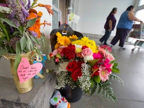 Shoppers push a cart past flowers and stuffed toys left in memorial to Addison Hall, the six-year-old girl who was killed Friday after a car reversed through the front doors of the Costco store on Wellington Road, in London, Ontario on Sunday July 27, 2014.  A Monte Carlo driven by a woman in her sixties suddenly backed into the entrance of the big-box store, reversing between two pillars before smashing through the glass doors and striking Danah McKinnon Bozek and her daughters Miah, 3, and Addison.  McKinnon Bozek's condition was upgraded to fair over the weekend, say police, however Miah and McKinnon Bozek's baby, who was delivered by emergency caesarian-section on Friday, remain in critical condition.  Police are investigating what caused the car to crash into the store and whether any charges will be laid against the driver.
CRAIG GLOVER/The London Free Press/QMI Agency