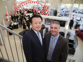 M.K. Kim, president and chief executive of Kia Canada, helps Ryan Brown celebrate the new location of his Kia dealership in London Thursday. (DEREK RUTTAN, The London Free Press)