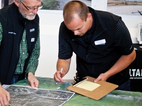 Two community liaisons from AltaLink look over a map and topographical model of the landscape involved in the company’s planned transmission line construction.