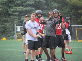 Henry Burris protects himself from the rain in a gathering of quarterbacks Thomas DeMarco, Derek Wendel and Hugo Richard with coach Don Yanowsky during a recent practice at Carleton University. (Tim Baines/Ottawa Sun)
