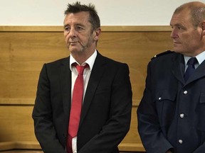 Former AC/DC drummer Phil Rudd (L) stands in in the dock flanked by security facing charges at the District Court in Tauranga, New Zealand on April 21, 2015. The veteran rocker made  a  surprise guilty plea on charges of threatening to kill and drug possession.  Rudd, 60,  had previously denied all allegations against him, but changed his plea on the first day of the trial at Tauranga District Court.

AFP PHOTO / MARTY MELVILLE