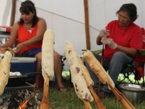Bannock is pressed onto sticks and placed near an outdoor fire to cook.