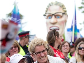 Ontario Premier Kathleen Wynne shakes hands with a member of the public as nearby OPSEU protesters carry an effigy of the provincial leader at the Pan Am Torch Relay in Victoria Park in London, Ont. on Wednesday June 17, 2015. Craig Glover/The London Free Press/Postmedia Network